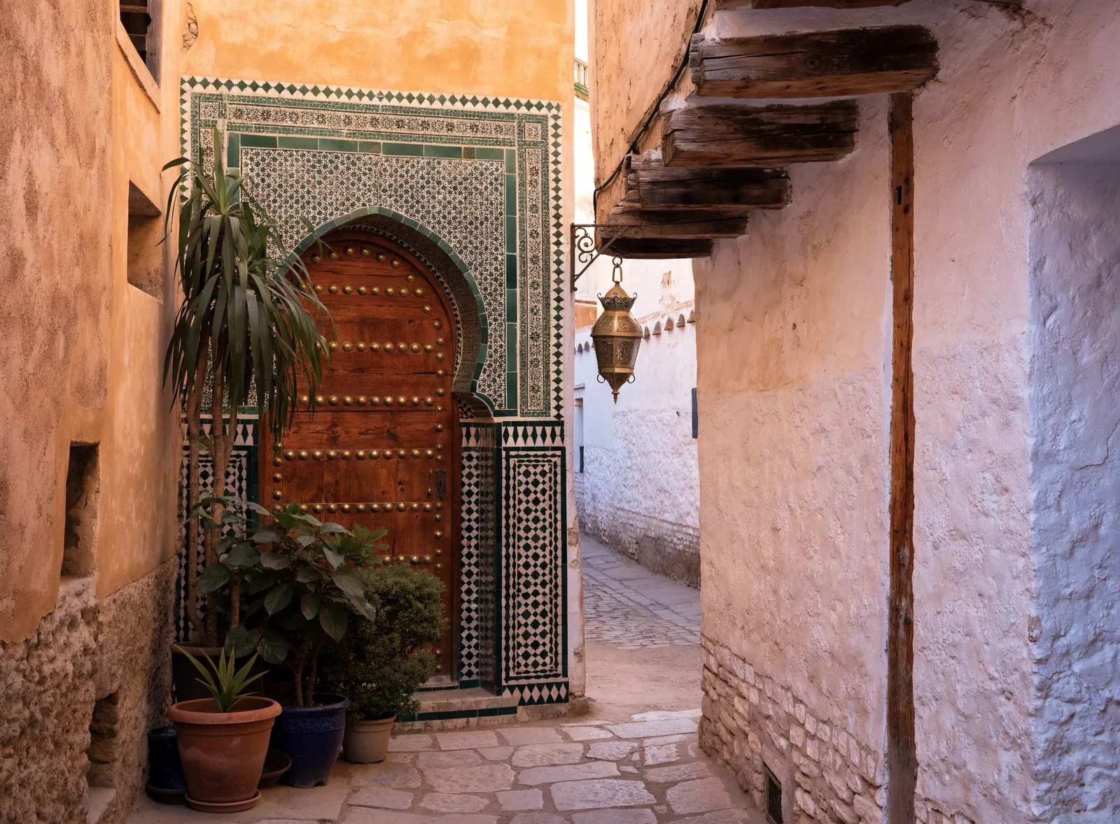 Illustrative image of a traditional riad entrance in the Fez medina, with a carved cedar door and zellige tiles.