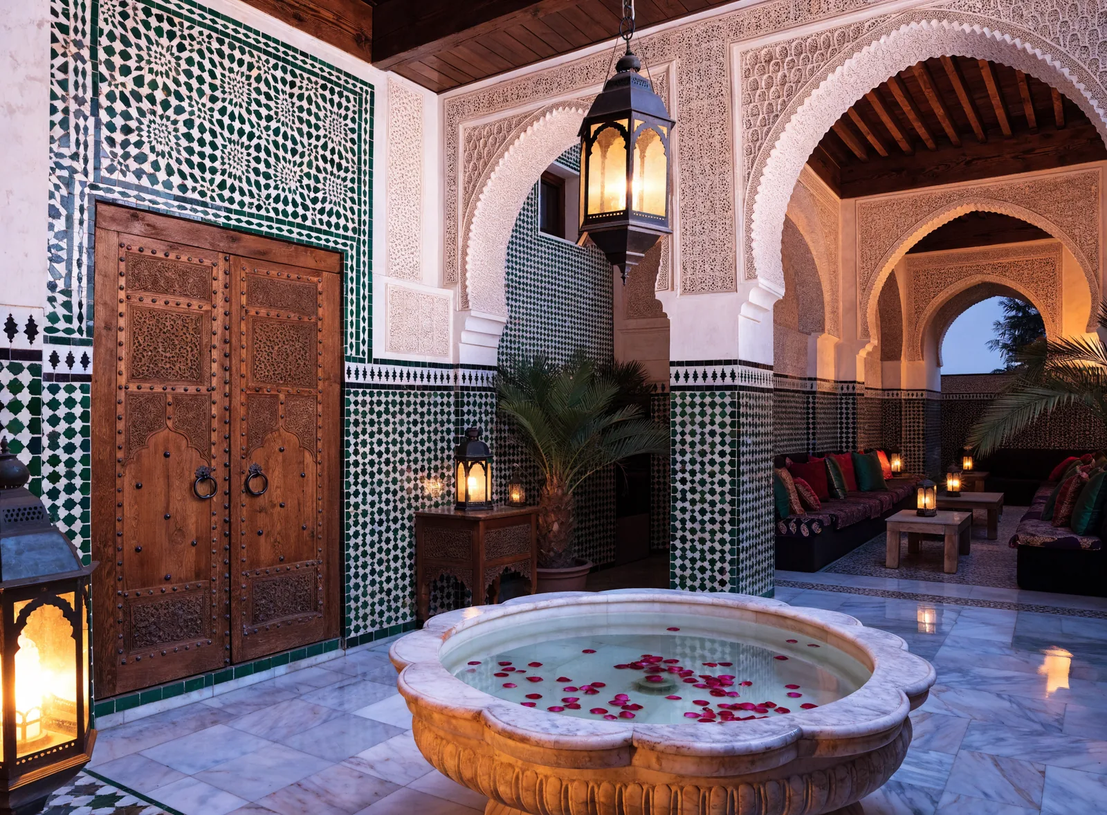 Illustrative image of a lantern-lit luxury riad courtyard in Fès el-Bali with a fountain, zellige and carved cedar doors.